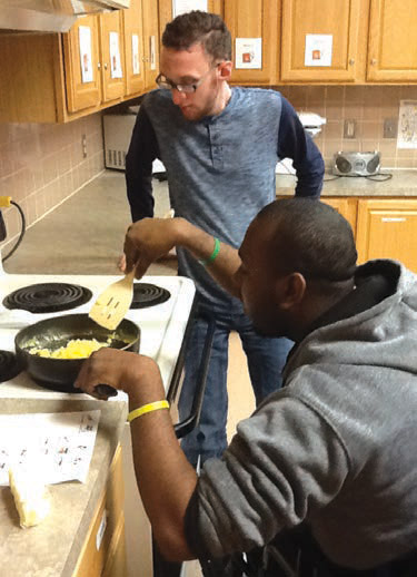 Larc student Darnail proudly and adeptly makes scrambled eggs while classmate, Kyle, observes, ready to lend a helping hand.